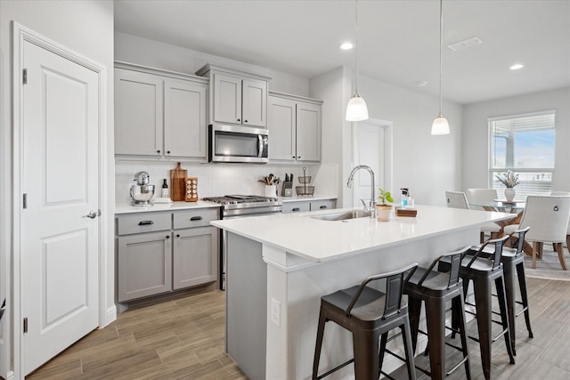 517 Big Horn Pass, Denton, TX 76210 - kitchen with stainless steel microwave, gray cabinets, a sink, decorative backsplash, and a kitchen breakfast bar