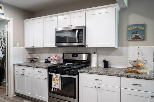 1306 S Oak Cliff Blvd, Dallas, TX 75208 - kitchen with appliances with stainless steel finishes, backsplash, white cabinetry, dark stone countertops, and wood finished floors