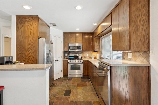 5020 Timber Creek Rd, Flower Mound, TX 75028 - kitchen featuring appliances with stainless steel finishes, dark stone finish floors, light countertops, tasteful backsplash, and brown cabinets