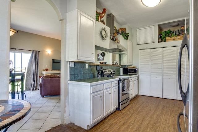 6980 Prather Rd, Springtown, TX 76082 - kitchen featuring appliances with stainless steel finishes, tile countertops, decorative backsplash, white cabinets, and arched walkways