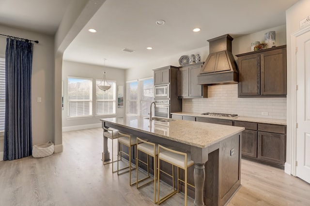 1305 Xeraco Dr, Little Elm, TX 75068 - kitchen with premium range hood, a sink, stainless steel appliances, light wood-style floors, and an island with sink