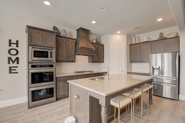 1305 Xeraco Dr, Little Elm, TX 75068 - kitchen with stainless steel appliances, a sink, custom exhaust hood, dark brown cabinetry, and light stone counters