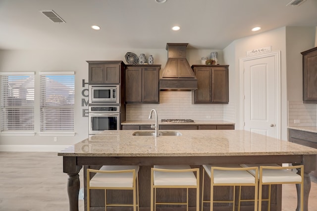 1305 Xeraco Dr, Little Elm, TX 75068 - kitchen with stainless steel appliances, custom exhaust hood, a sink, backsplash, and a breakfast bar