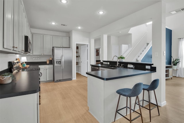1356 Portsmouth Dr, Providence Village, TX 76227 - kitchen featuring appliances with stainless steel finishes, a sink, dark countertops, light wood finished floors, and a breakfast bar area