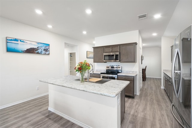 100 Samuel St, Denton, TX 76207 - kitchen featuring stainless steel appliances, light wood-type flooring, baseboards, an island with sink, and dark brown cabinetry