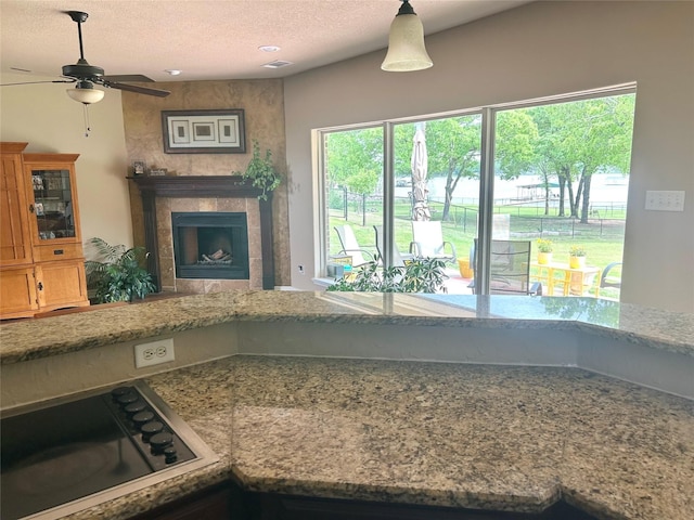2663 Rodeo Dr, Quinlan, TX 75474 - kitchen featuring a tile fireplace, black electric cooktop, ceiling fan, a textured ceiling, and stone counters