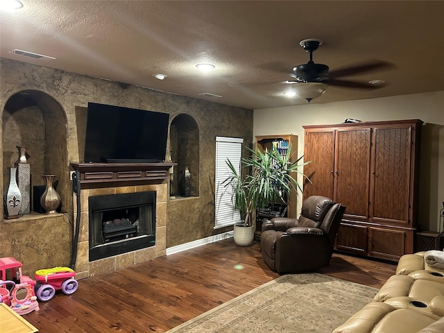2663 Rodeo Dr, Quinlan, TX 75474 - living area featuring wood finished floors, a ceiling fan, a tiled fireplace, baseboards, and arched walkways