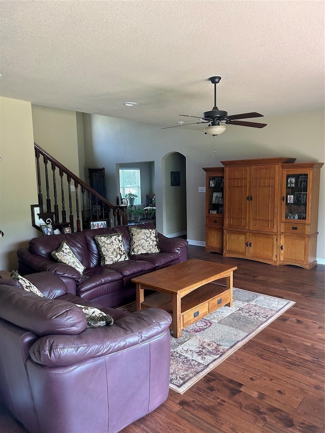 2663 Rodeo Dr, Quinlan, TX 75474 - living room featuring arched walkways, a ceiling fan, dark wood-style flooring, a textured ceiling, and stairs