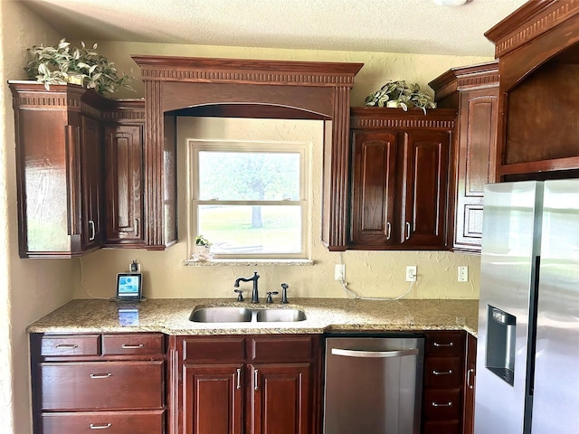 2663 Rodeo Dr, Quinlan, TX 75474 - kitchen featuring appliances with stainless steel finishes, a sink, a textured ceiling, light stone countertops, and reddish brown cabinets