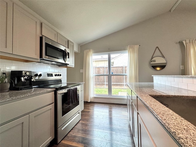 6014 Mcafee Dr, The Colony, TX 75056 - kitchen featuring appliances with stainless steel finishes, lofted ceiling, backsplash, dark wood finished floors, and light stone countertops