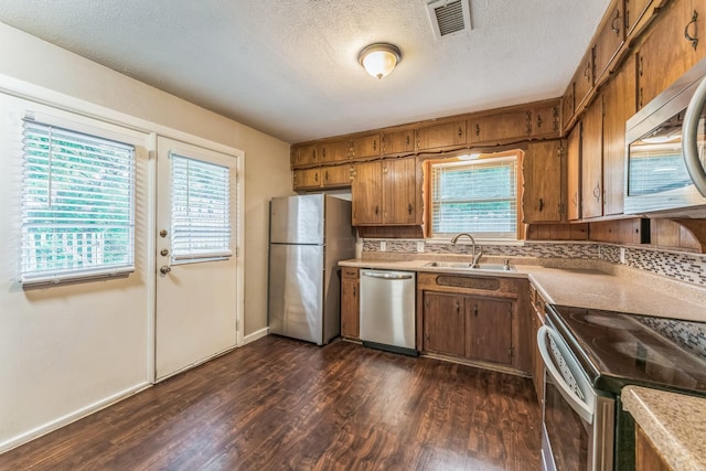 311 Franklin Dr, Euless, TX 76040 - kitchen with appliances with stainless steel finishes, a sink, brown cabinetry, light countertops, and dark wood-style floors