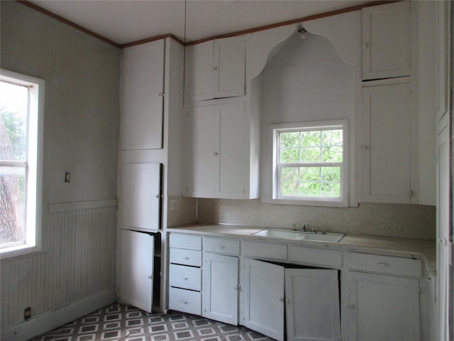 1203 Sewanee Dr, Marlin, TX 76661 - kitchen with a sink, white cabinetry, light countertops, a wainscoted wall, and tile patterned floors