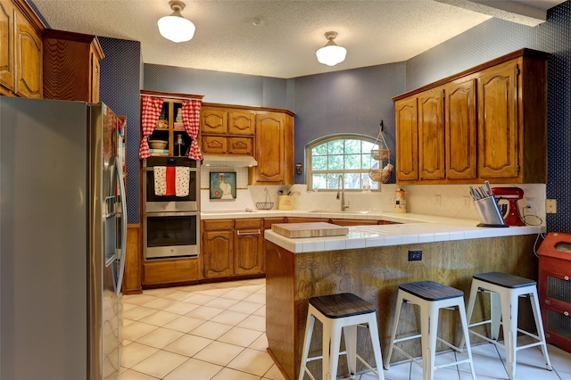 3908 Jamestown Pl, Plano, TX 75023 - kitchen with stainless steel appliances, a peninsula, a sink, brown cabinets, and a kitchen bar