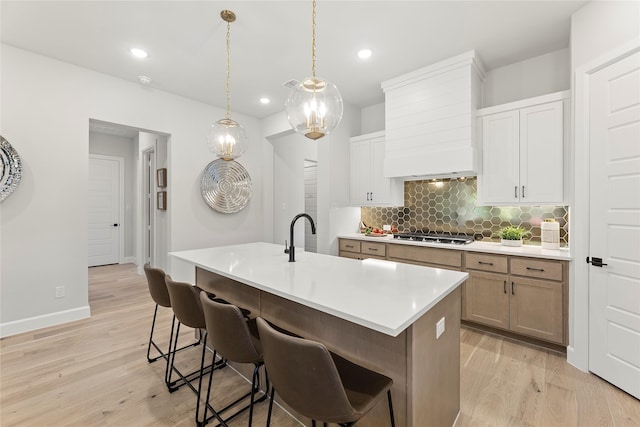 1044 Olympic Dr, Rockwall, TX 75087 - kitchen featuring tasteful backsplash, light wood-type flooring, premium range hood, a sink, and a breakfast bar area