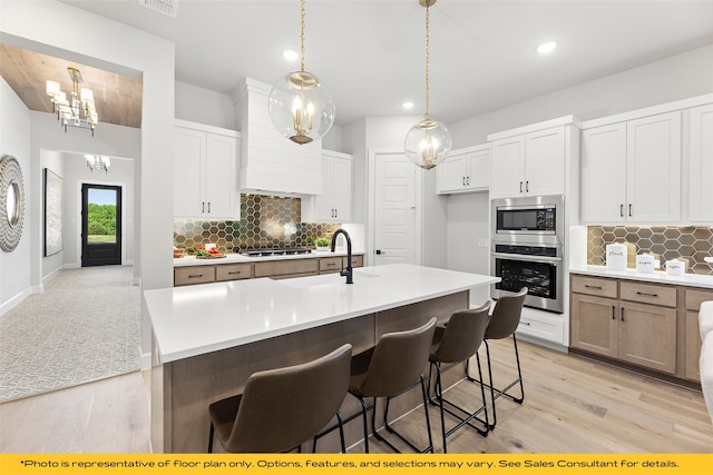 1044 Olympic Dr, Rockwall, TX 75087 - kitchen with stainless steel appliances, a sink, wall chimney range hood, a chandelier, and light wood-type flooring