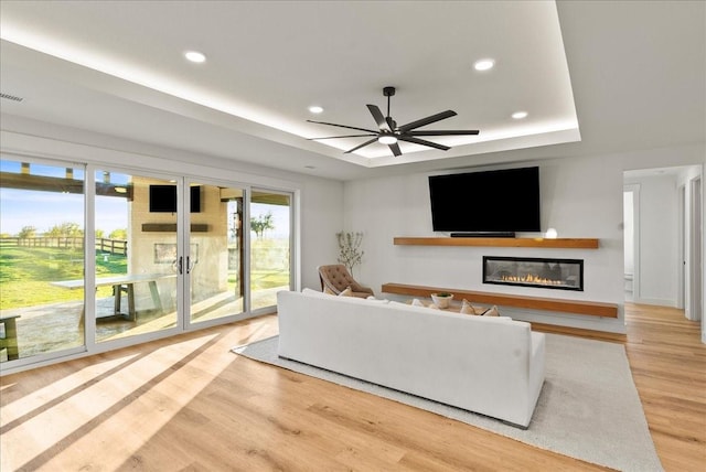 3417 Dovehill Dr, Northlake, TX 76247 - living room with a raised ceiling, a glass covered fireplace, light wood finished floors, a ceiling fan, and recessed lighting