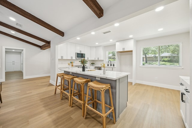 37 Devonshire Dr, Bedford, TX 76021 - kitchen featuring stainless steel microwave, baseboards, light stone counters, a kitchen island, and white cabinetry