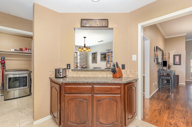 2510 High Pointe Blvd, Mckinney, TX 75071 - kitchen with brown cabinetry, light stone counters, washer / clothes dryer, a chandelier, and crown molding