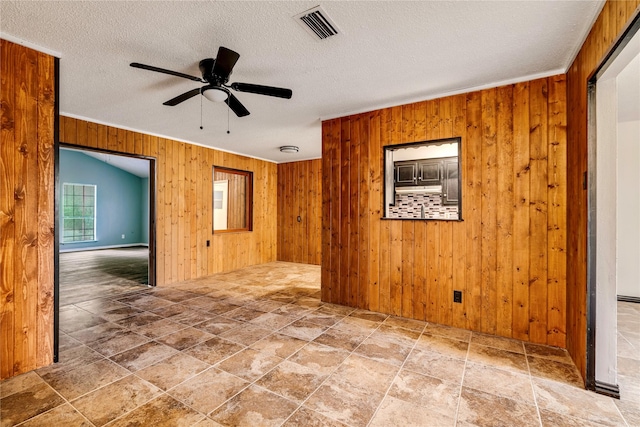 635 N Center St, Blossom, TX 75416 - unfurnished room with wood walls, a ceiling fan, ornamental molding, a textured ceiling, and stone finish floors