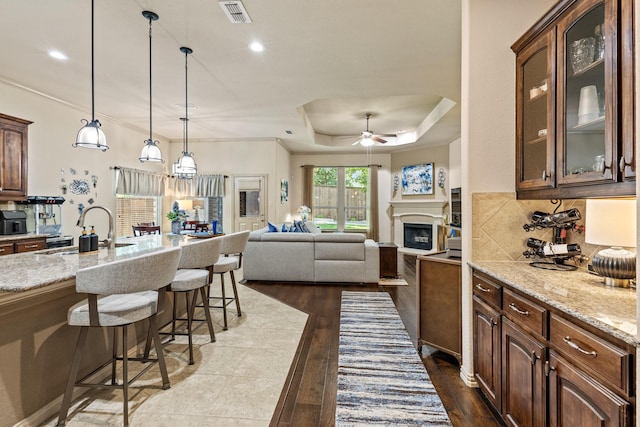 2508 Pioneer Dr, Denton, TX 76210 - kitchen featuring a sink, a kitchen breakfast bar, a raised ceiling, a ceiling fan, and light stone counters
