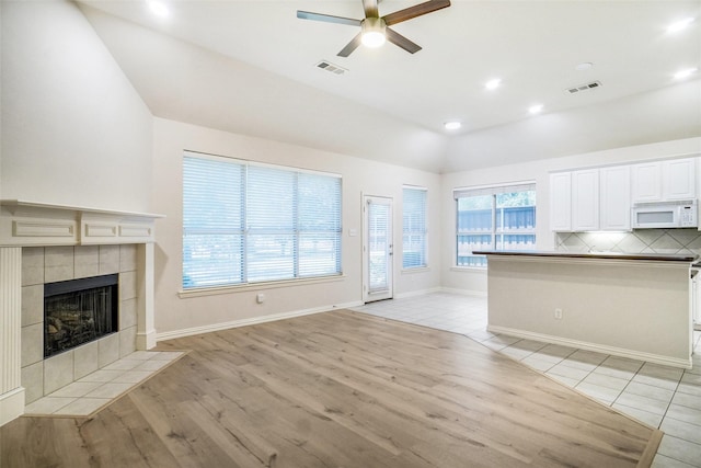 8393 Davis Dr, Frisco, TX 75036 - unfurnished living room featuring vaulted ceiling, light wood-style flooring, a ceiling fan, a tile fireplace, and baseboards