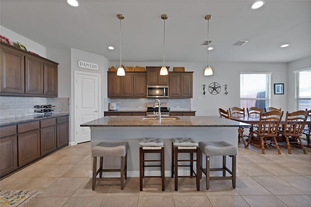 1099 Admiral Dr, Azle, TX 76020 - kitchen with stainless steel microwave, a breakfast bar area, decorative backsplash, a center island with sink, and light tile patterned flooring