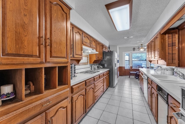 227 Meadowlark Ln, Duncanville, TX 75137 - kitchen with a textured ceiling, a sink, brown cabinetry, under cabinet range hood, and tasteful backsplash