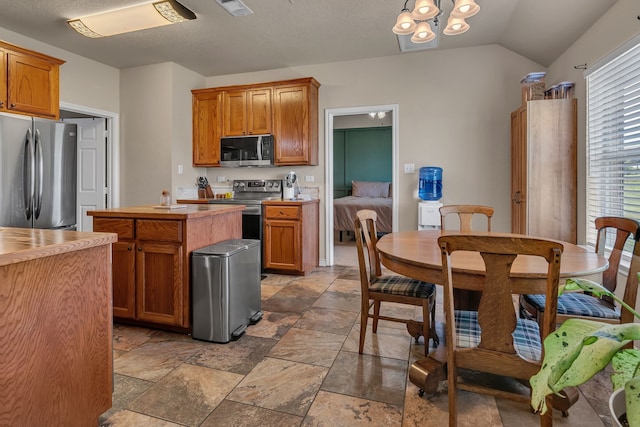 111 Ladonna Ct, Decatur, TX 76234 - kitchen featuring appliances with stainless steel finishes, stone tile flooring, light countertops, lofted ceiling, and brown cabinets