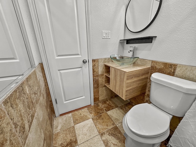 3837 Finley Rd, Irving, TX 75062 - bathroom with tile walls, stone tile flooring, vanity, toilet, and wainscoting