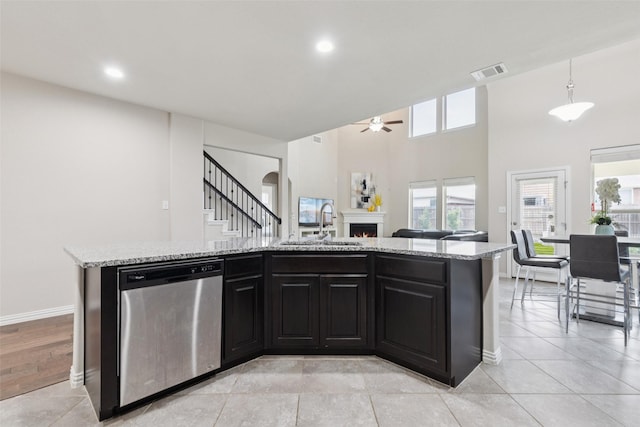 824 Water Garden Cir, Little Elm, TX 75068 - kitchen with stainless steel dishwasher, a lit fireplace, ceiling fan, light stone countertops, and a kitchen island with sink