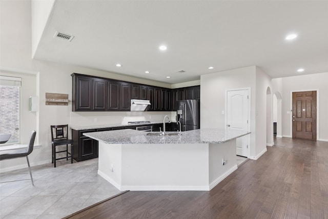 824 Water Garden Cir, Little Elm, TX 75068 - kitchen with stainless steel fridge with ice dispenser, arched walkways, a center island with sink, range, and light stone countertops