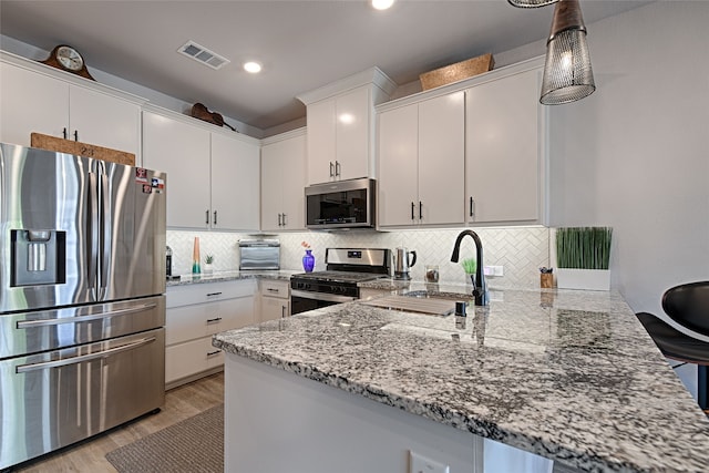 841 Emerling Dr, Mckinney, TX 75069 - kitchen featuring appliances with stainless steel finishes, a peninsula, light stone countertops, white cabinetry, and decorative backsplash