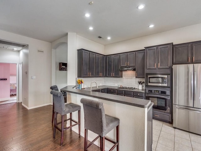 1676 Castle Pines Dr, Frisco, TX 75036 - kitchen featuring appliances with stainless steel finishes, a peninsula, a breakfast bar area, tasteful backsplash, and recessed lighting