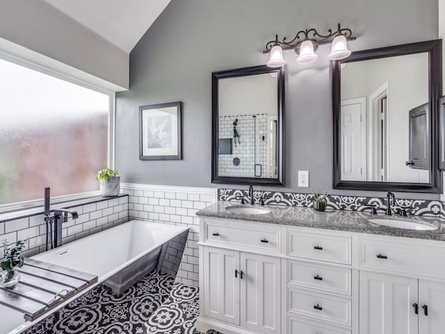 1676 Castle Pines Dr, Frisco, TX 75036 - bathroom with vaulted ceiling, a soaking tub, double vanity, tile walls, and tile patterned flooring
