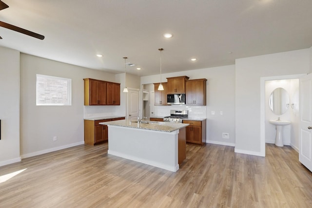 1808 Summer Aura, Mesquite, TX 75181 - kitchen featuring stainless steel appliances, brown cabinets, ceiling fan, light wood-type flooring, and a center island with sink