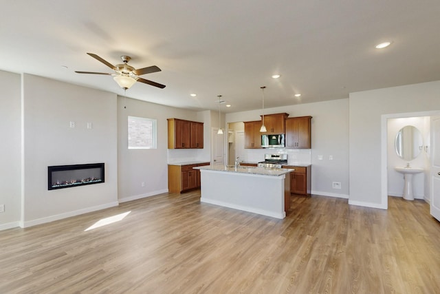 1804 Summer Aura, Mesquite, TX 75181 - kitchen featuring appliances with stainless steel finishes, a glass covered fireplace, a ceiling fan, brown cabinets, and light wood-type flooring