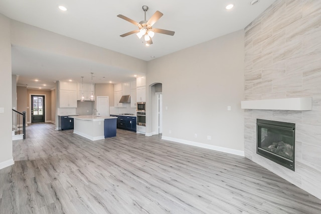 2033 Barbette St, Fort Worth, TX 76008 - unfurnished living room with light wood finished floors, a tiled fireplace, a ceiling fan, arched walkways, and recessed lighting