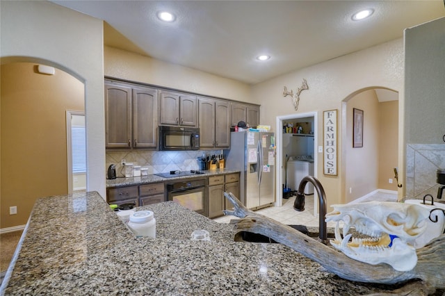 144 Brady Coleman Ln, Springtown, TX 76082 - kitchen with black appliances, arched walkways, washer / dryer, light stone counters, and tasteful backsplash