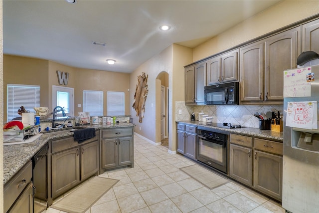144 Brady Coleman Ln, Springtown, TX 76082 - kitchen featuring black appliances, arched walkways, light tile patterned floors, decorative backsplash, and light stone countertops