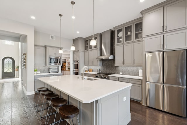 925 Glen Lake Dr, Southlake, TX 76092 - kitchen featuring appliances with stainless steel finishes, wall chimney exhaust hood, gray cabinets, dark wood-style flooring, and a center island with sink