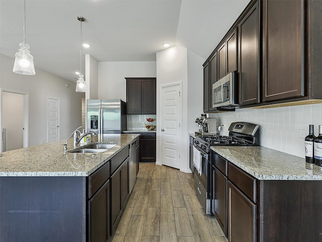 2624 Rambling Rd, Celina, TX 75009 - kitchen with stainless steel appliances, dark brown cabinets, wood finished floors, a kitchen island with sink, and light stone countertops