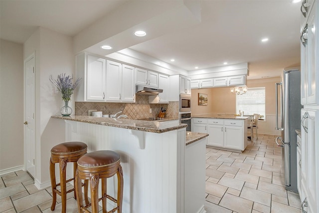 8921 Crest Ridge Dr, Fort Worth, TX 76179 - kitchen with a peninsula, white cabinets, appliances with stainless steel finishes, light stone countertops, and backsplash