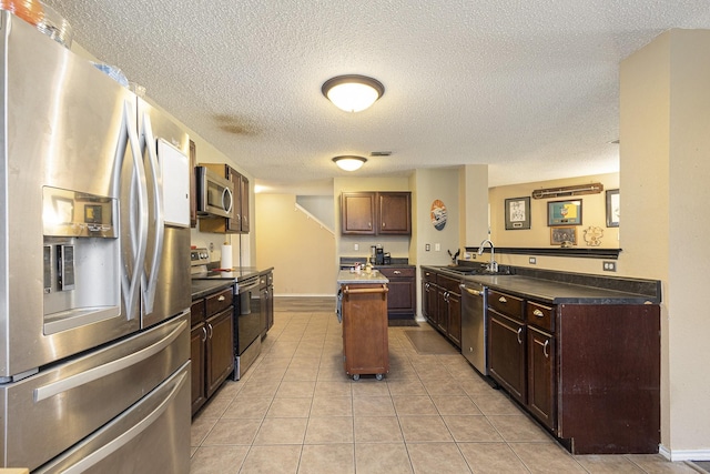 1400 Sunflower Ct, Burleson, TX 76028 - kitchen featuring appliances with stainless steel finishes, a sink, a textured ceiling, a kitchen island, and light tile patterned floors