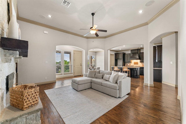 647 Gillon Way, Rockwall, TX 75087 - living area featuring arched walkways, a ceiling fan, a stone fireplace, crown molding, and dark wood finished floors