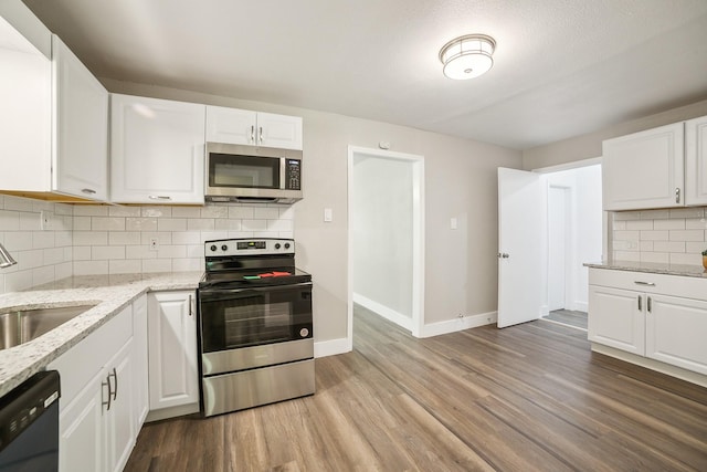 841 20th St SE, Paris, TX 75460 - kitchen with appliances with stainless steel finishes, a sink, baseboards, light wood-style floors, and white cabinetry