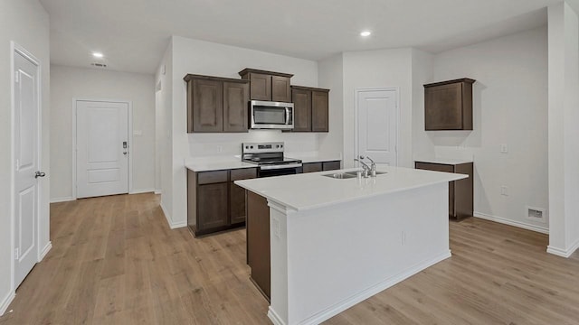 434 Drake Dr, Ferris, TX 75125 - kitchen featuring appliances with stainless steel finishes, light wood finished floors, dark brown cabinets, an island with sink, and recessed lighting