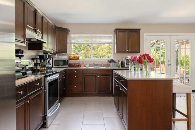 2300 Ash Grove Trl, Fort Worth, TX 76112 - kitchen with under cabinet range hood, stainless steel appliances, light tile patterned floors, a kitchen island, and a kitchen bar