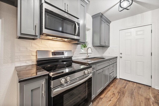 1111 N 11th St, Waco, TX 76707 - kitchen with appliances with stainless steel finishes, gray cabinets, a sink, decorative backsplash, and wood finished floors