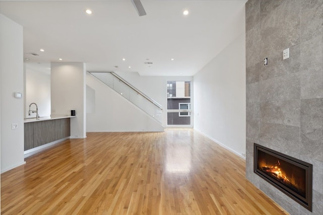 2706 Throckmorton St Unit C, Dallas, TX 75219 - unfurnished living room featuring a tile fireplace, light wood finished floors, stairs, recessed lighting, and baseboards