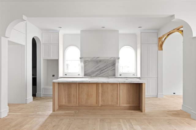 6207 Marquita Ave, Dallas, TX 75214 - kitchen with arched walkways, light wood-style flooring, white cabinetry, a center island, and light countertops